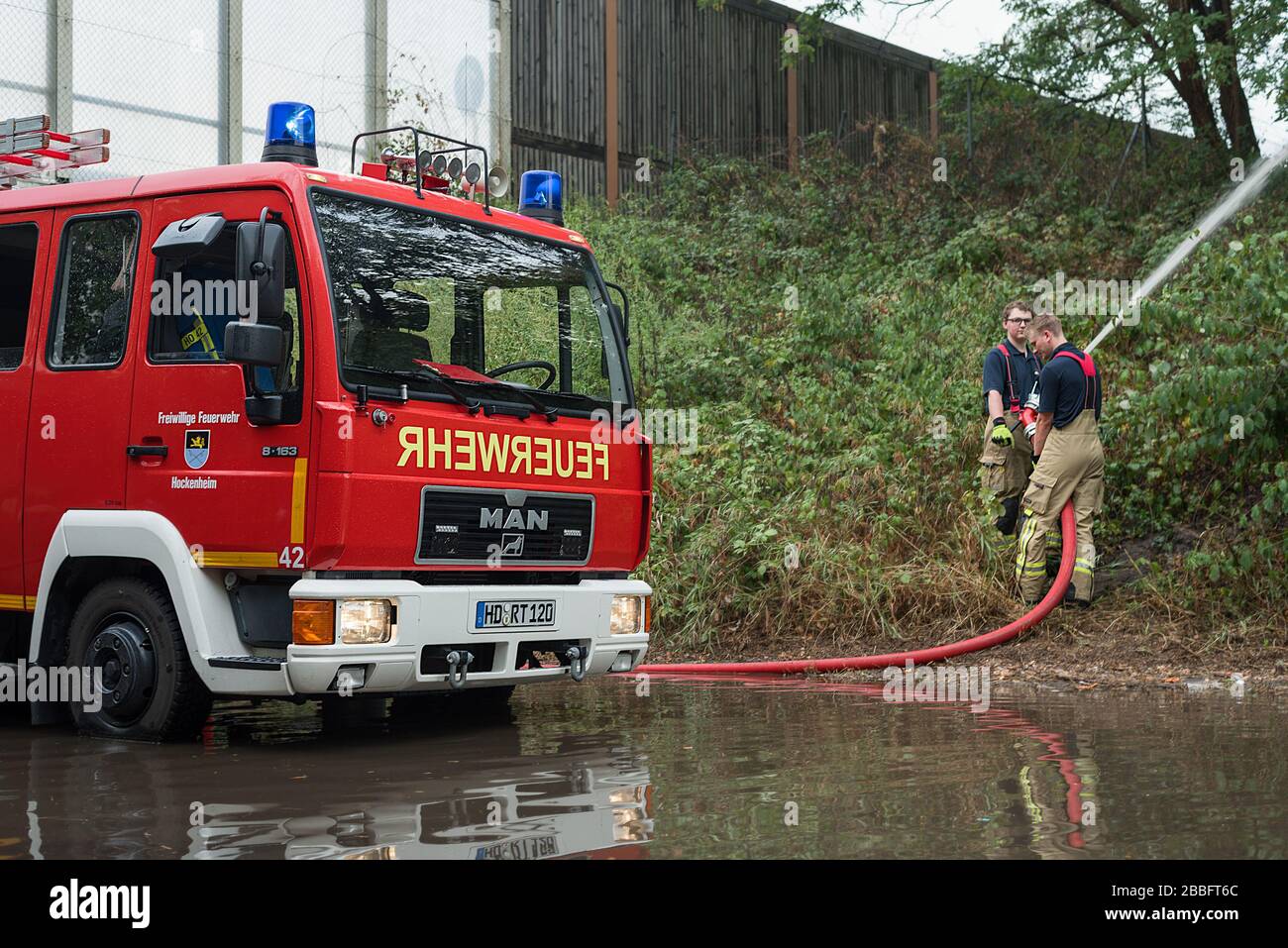 Dos personal de bomberos de los servicios de emergencia ayudan a bombear agua de inundación desde una carretera con sus poderosas bombas camiones de bomberos rojos. Foto de stock