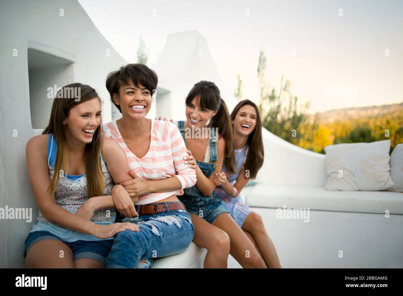 Cuatro amigos sonrientes sentados en un balcón Foto de stock