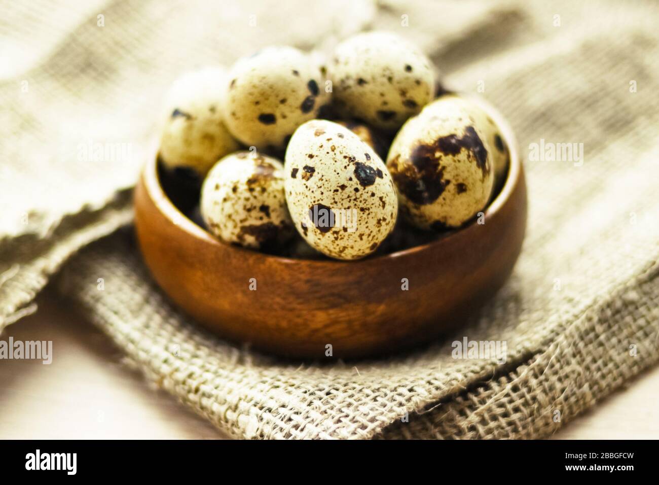 Codore los huevos en un cuenco de bambú redondo sobre lienzo de saco sobre fondo de madera. Alimentación saludable, concepto de Pascua. Foto de stock