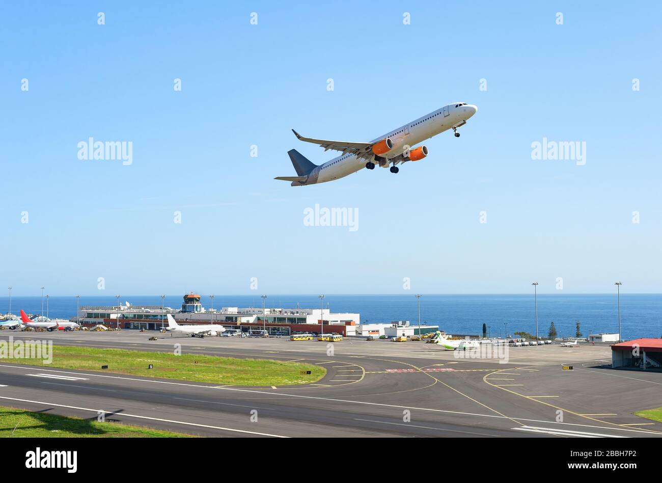Avión despegando de la pista de aterrizaje en el aeropuerto internacional de Madeira, la construcción de la terminal y el paisaje marino en el fondo, Portugal Foto de stock