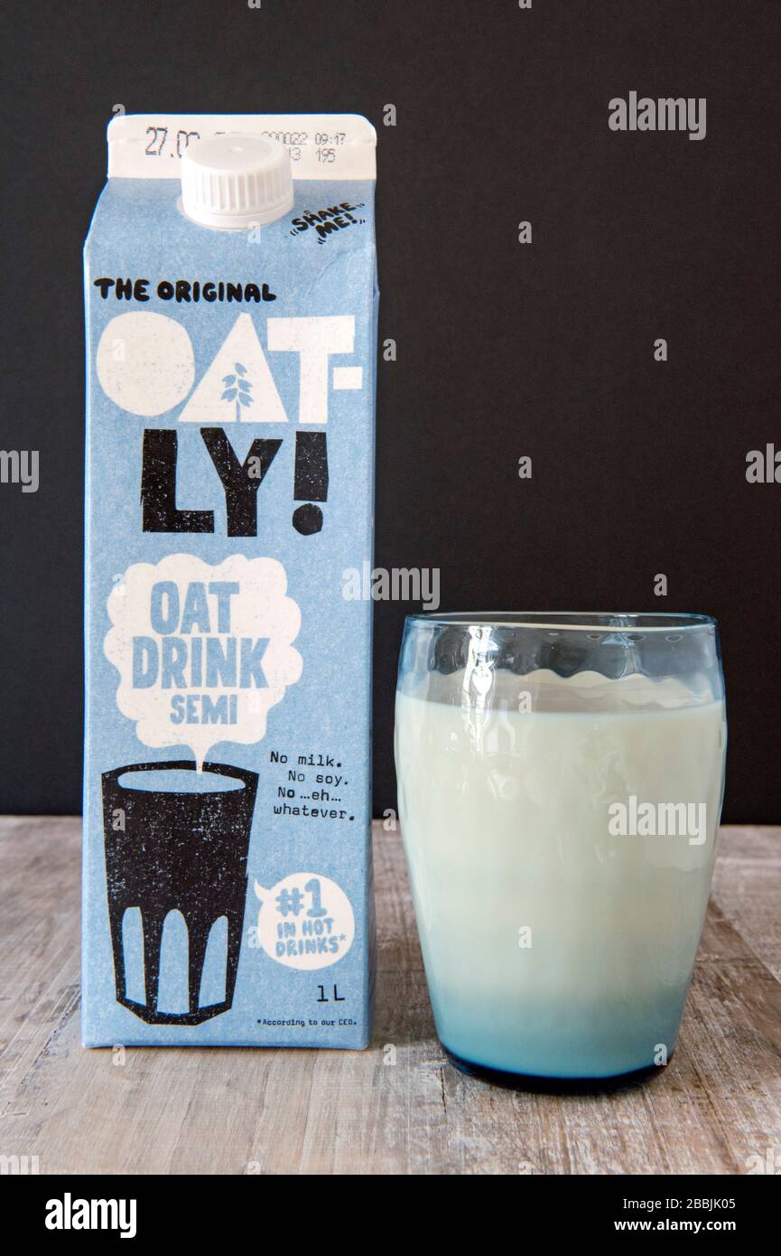 Vegan Oatly Oat bebida de leche en vidrio azul vintage con el original Oatly avena bebida cartón detrás con fondo negro. Sólo para uso editorial. Foto de stock