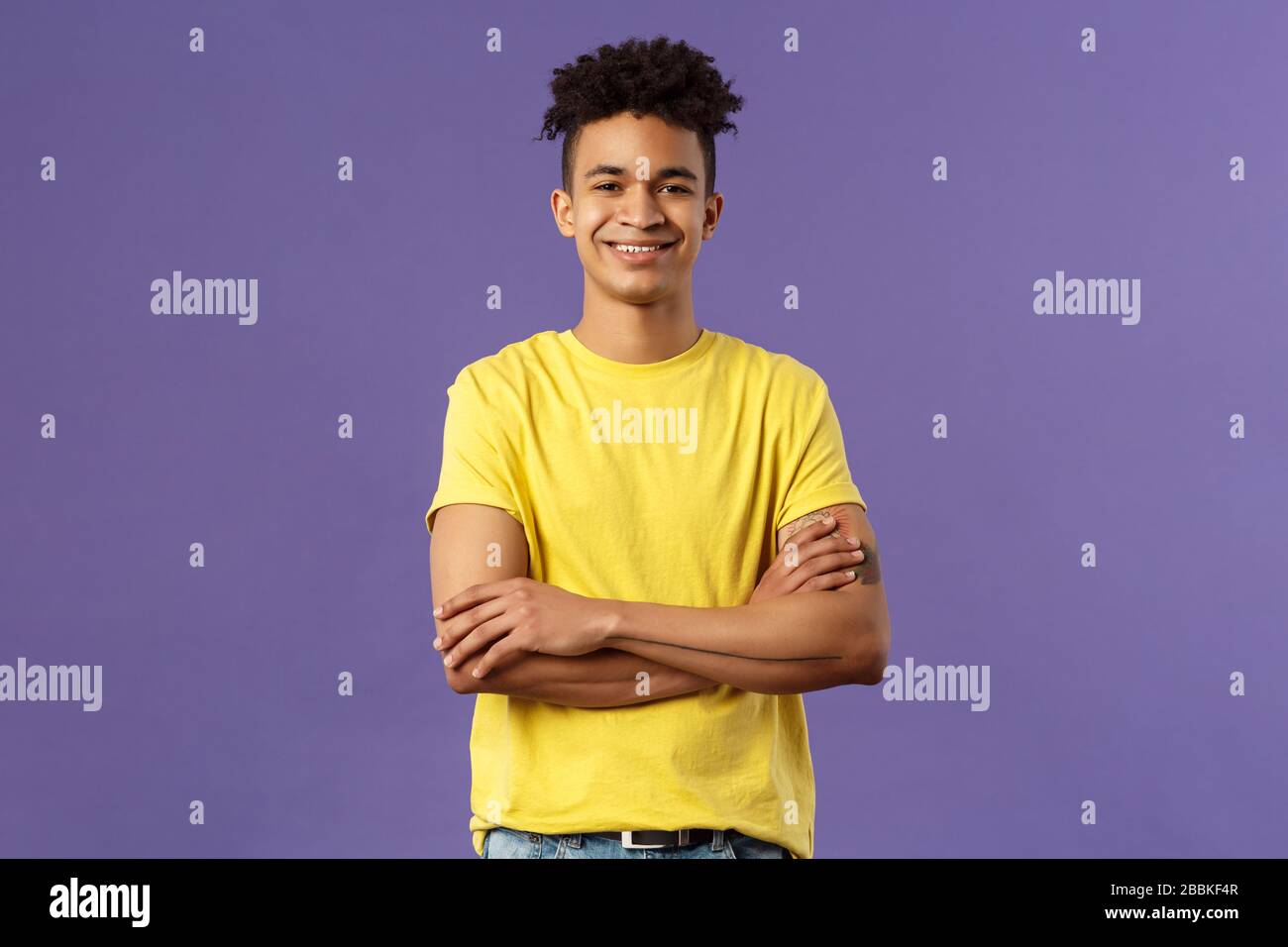 Retrato de primer plano de un joven estudiante profesional, inteligente y seguro con dreadlocks, camiseta amarilla, brazos cruzados sobre el pecho y una sonrisa feliz Foto de stock