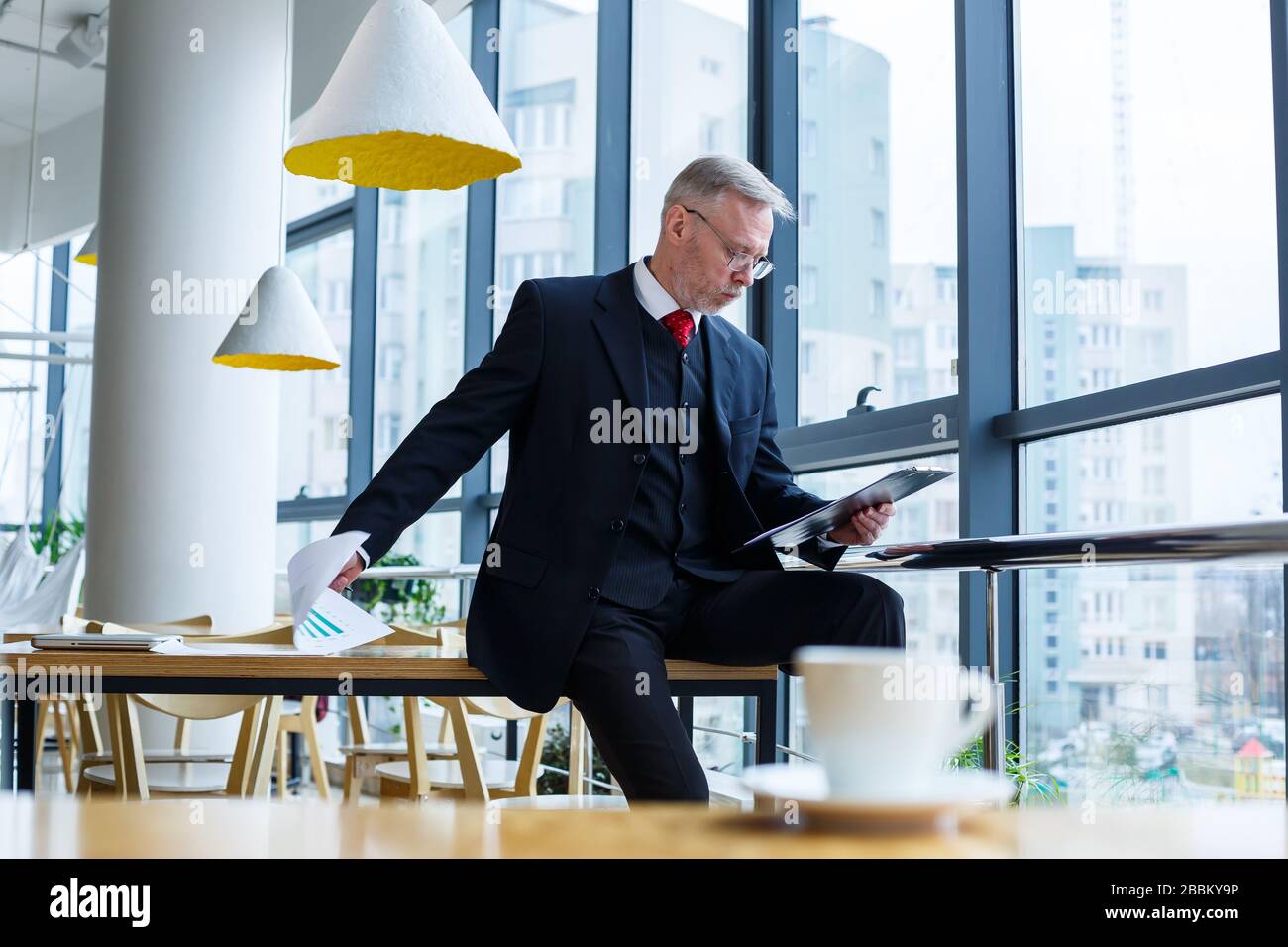 El director general del hombre se inclinó sobre una mesa de madera en su oficina cerca de una ventana grande y observa un plan de desarrollo empresarial exitoso. Foto de stock