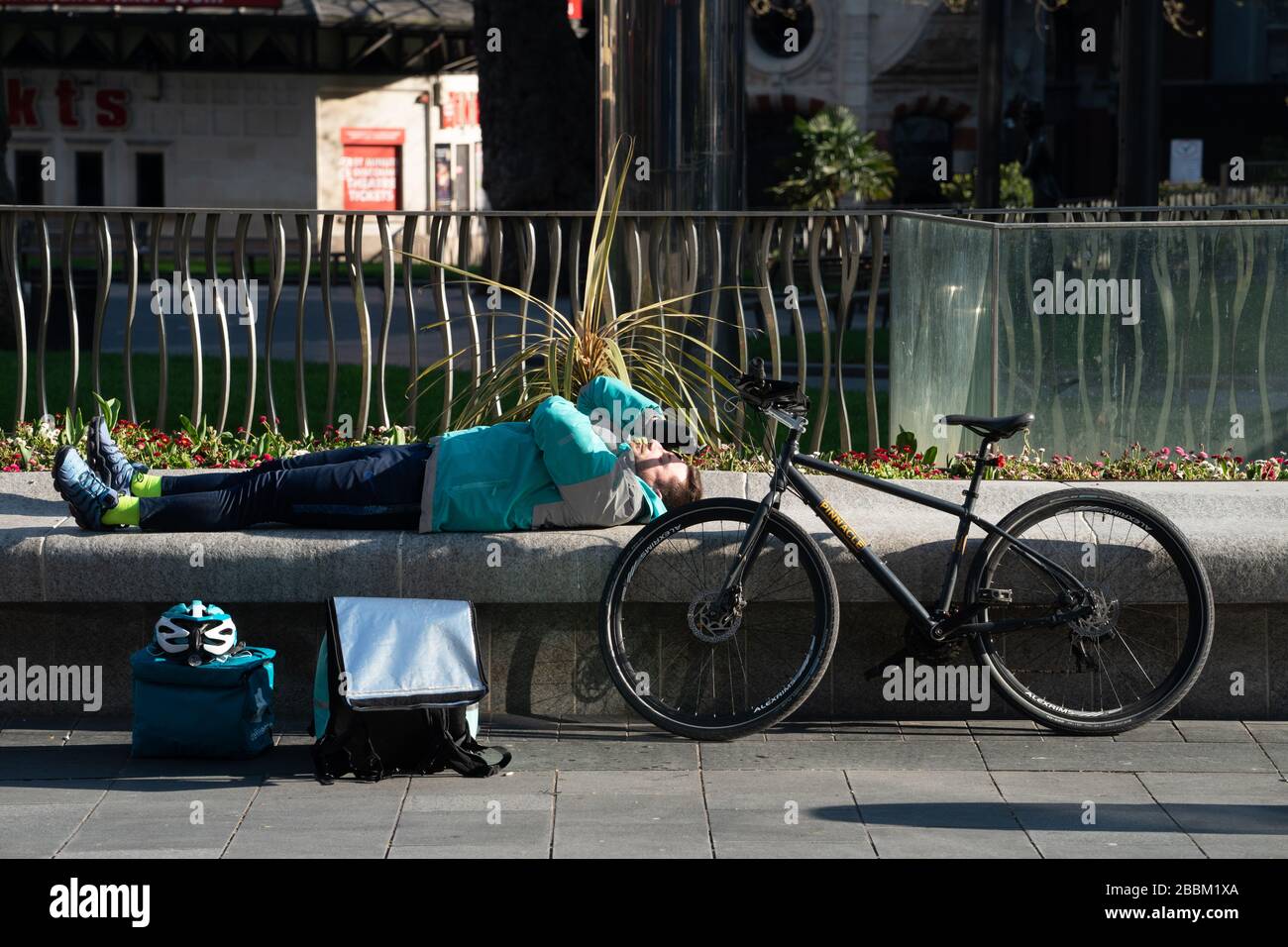 Un jinete de Delipoo toma un descanso en una Leicester Square, casi desierta, en el centro de Londres, después de que el gobierno declarara un cierre parcial en el Reino Unido. Fot Foto de stock