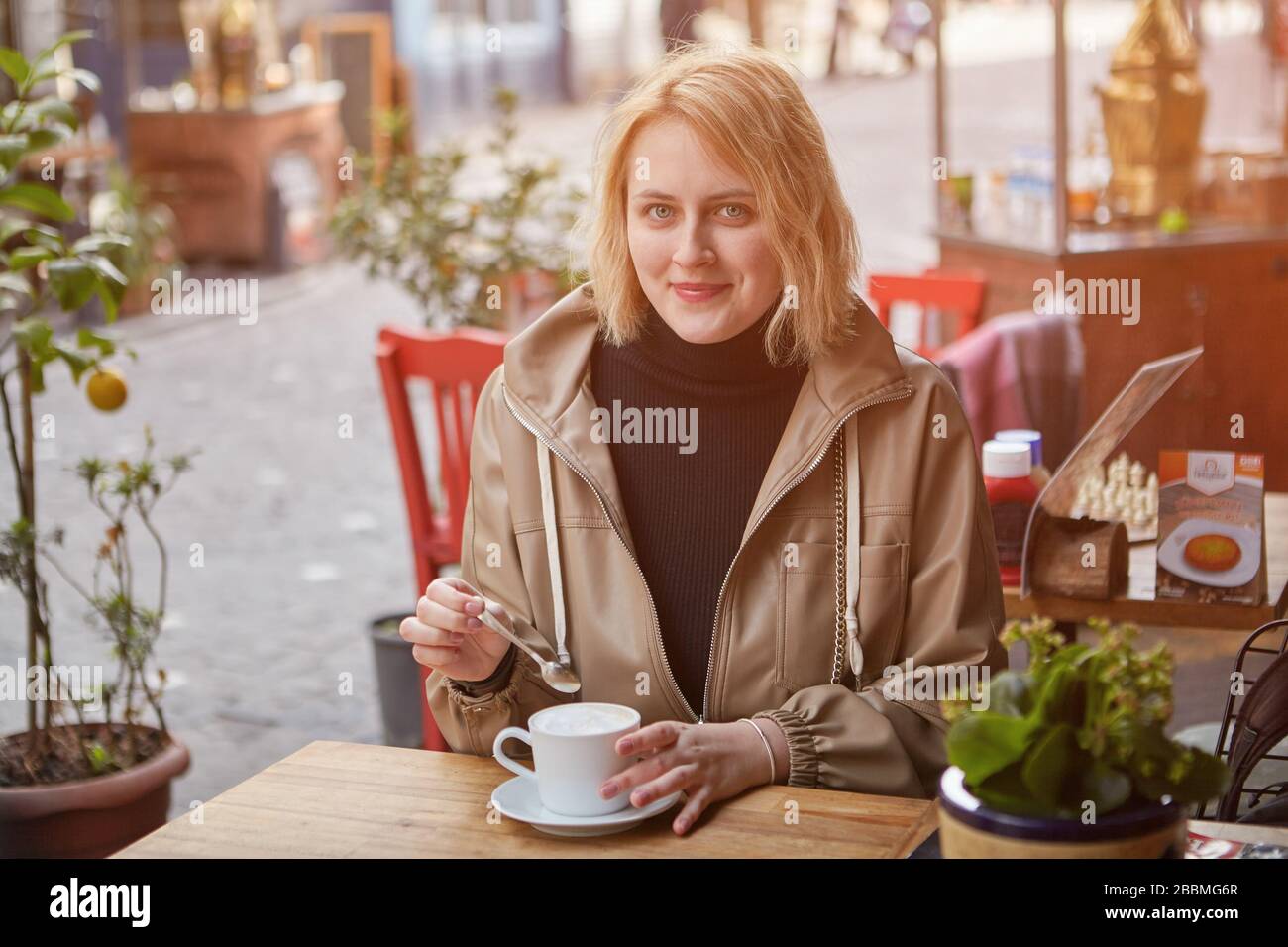 Una joven mujer caucásica sonriente se está relajando en un café de la calle en Estambul con una taza de café. Mujeres blancas viajan a Turquía. Foto de stock