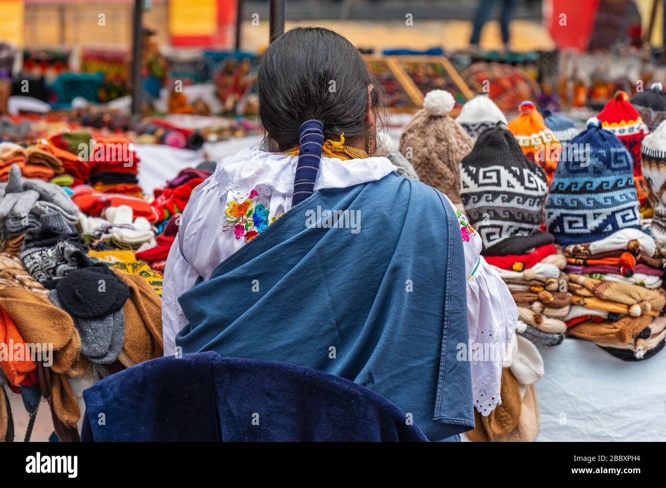 Las mujeres indígenas en ropa tradicional y peinado por su mercado se estancan en el mercado de arte y artesanía dominical de Otavalo, al norte de Quito, Ecuador. Foto de stock