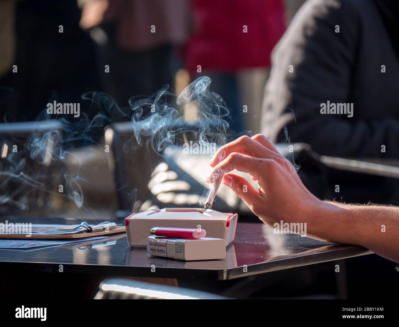 Mujer mano sosteniendo el cigarrillo con humo en la mesa. Fumar adicción a la nicotina estilo de vida malsano. Foto de stock