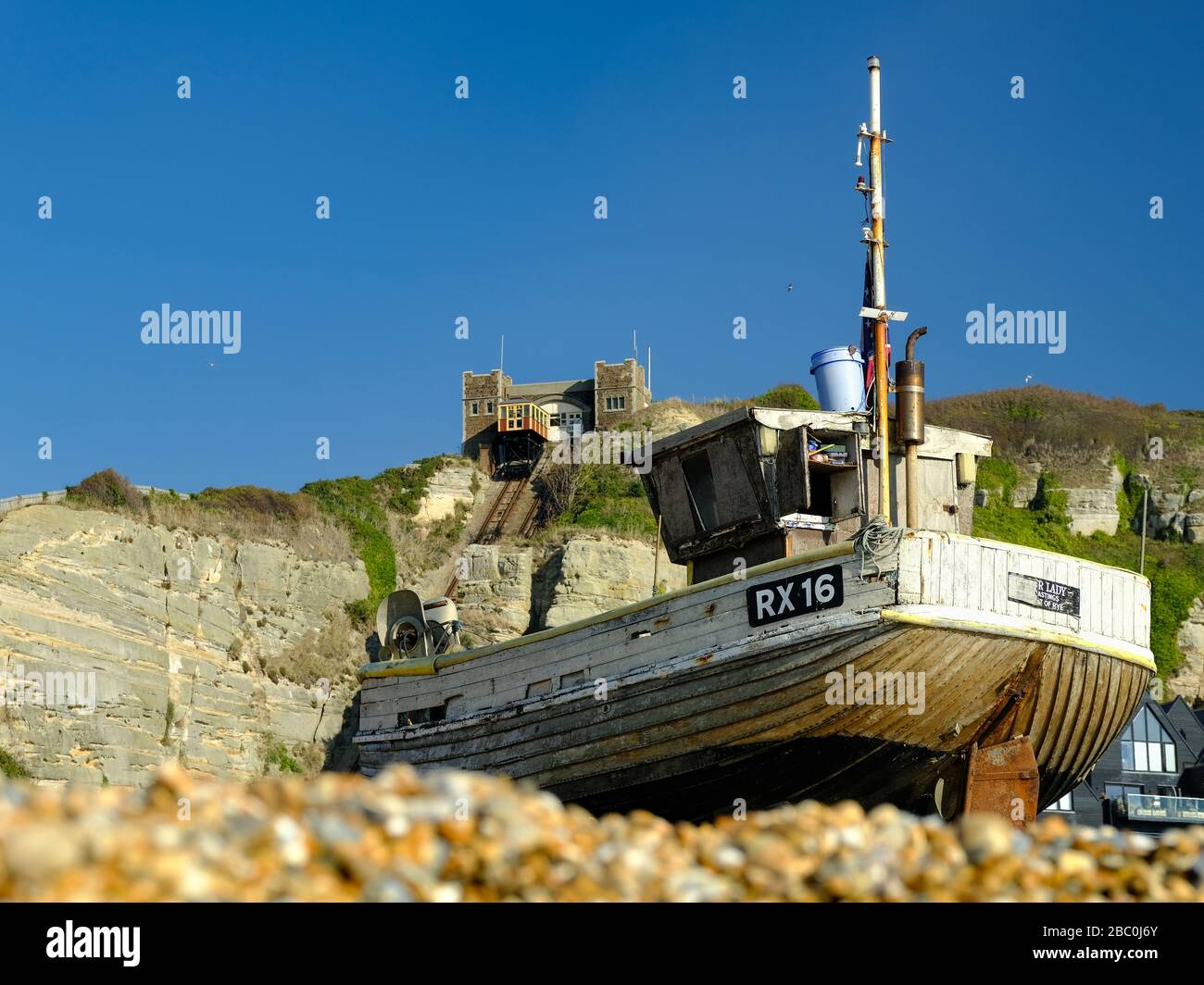 Barco de pesca en la playa de guijarros en Hastings, Reino Unido, con el funicular al fondo Foto de stock