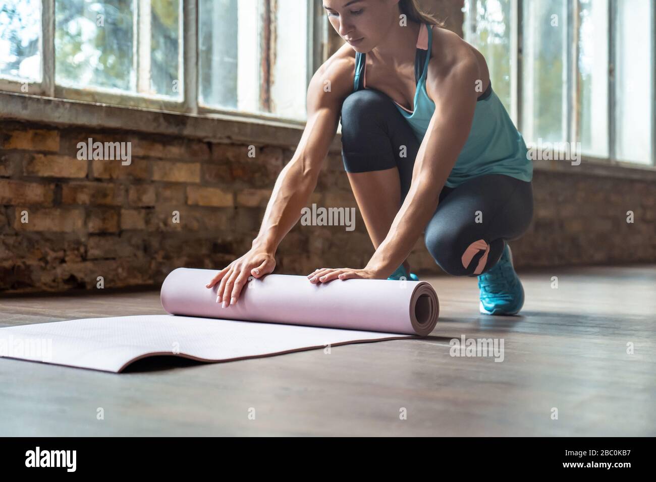 Ajuste deportivo mujer instructor de yoga llevar ropa deportiva rodillo desenrollar colchoneta de yoga en el gimnasio. Foto de stock