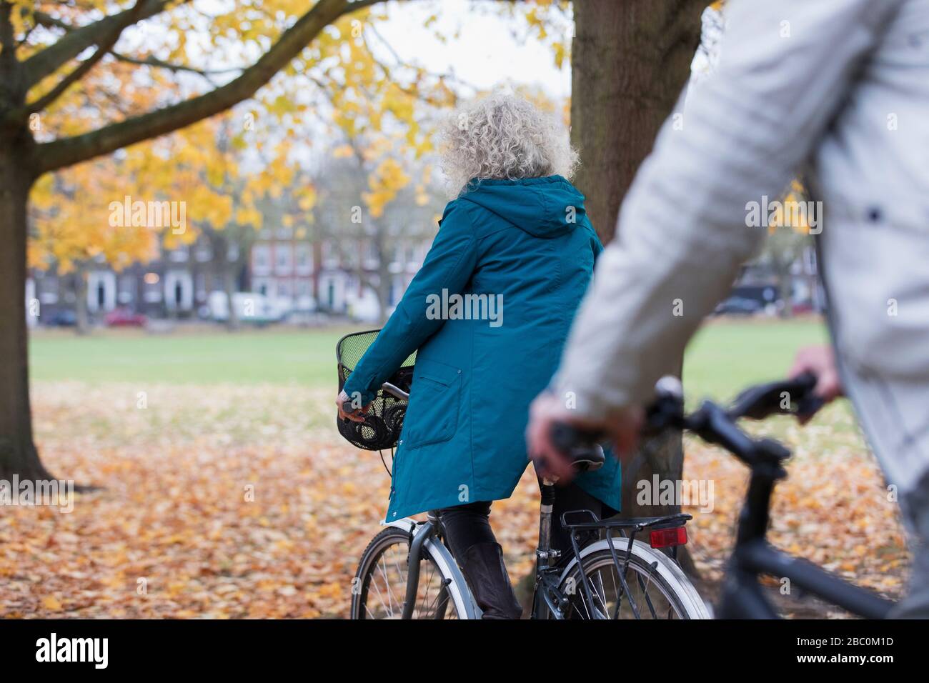 Mujer mayor montar en bicicleta entre las hojas de otoño en el parque Foto de stock