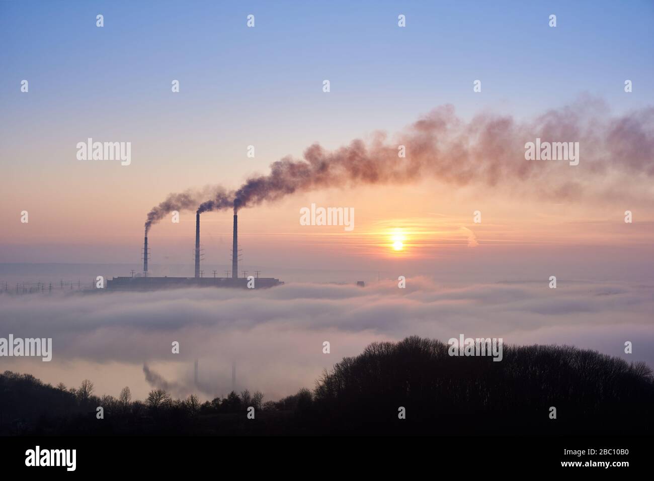 Instantánea horizontal de tres pilas de humo de la central térmica en el horizonte tomado de la colina, las tuberías están en la niebla de la noche en el cielo azul, espacio de copia. Concepto de contaminación ambiental Foto de stock