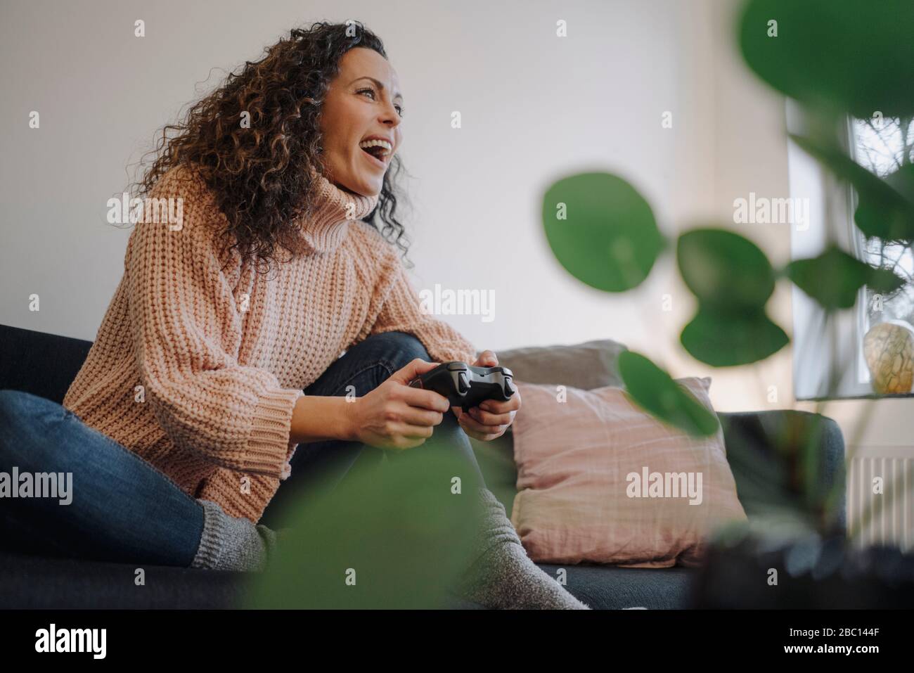 Mujer sentada en el sofá, divirtiéndose, jugando con una consola de juegos Foto de stock