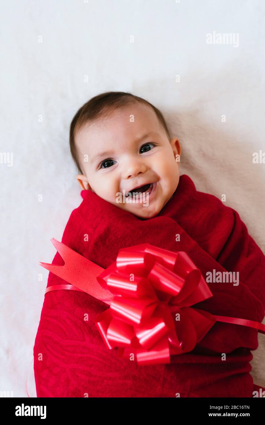 Retrato de niña feliz envuelto como regalo de Navidad con cinta roja sobre fondo blanco Foto de stock