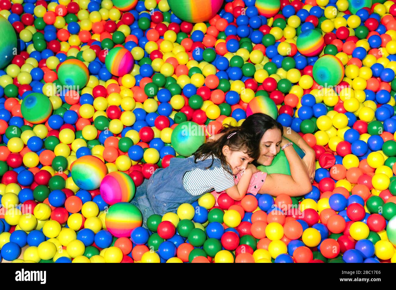 Mujer feliz acostada con su hija pequeña entre muchas bolas coloridas Foto de stock