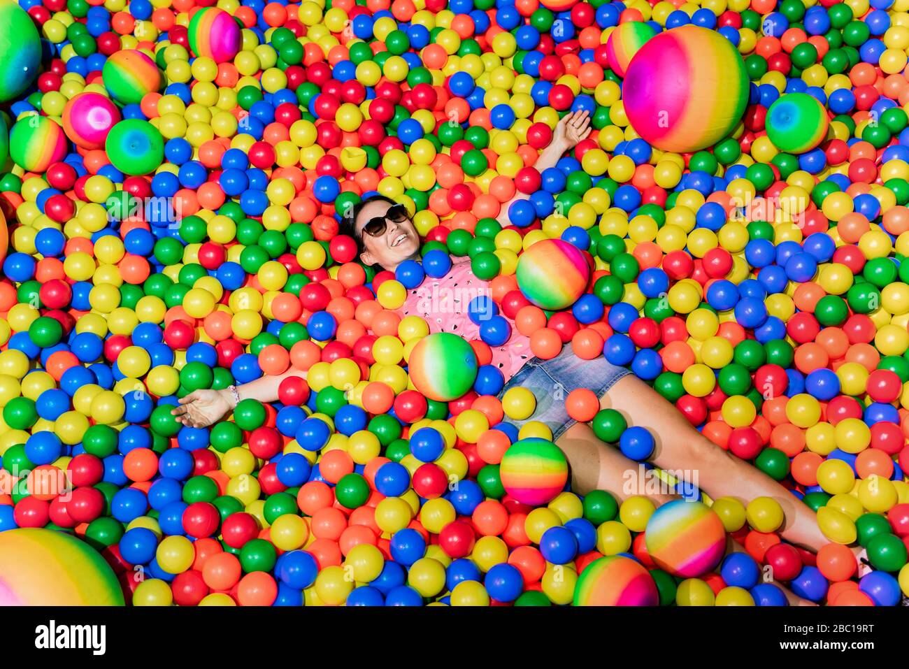 Retrato de una mujer feliz acostada entre muchas bolas de colores Foto de stock