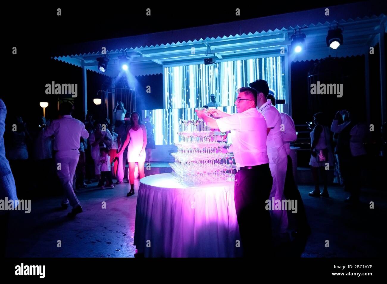 Tekirova, Turquía - 20 de octubre de 2019: Los gerentes de hotel en trajes blancos vierten champán en vasos. Fiesta blanca en el hotel Club Phaselis Rose en Kemer, d Foto de stock