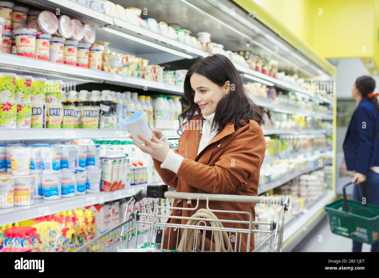 Mujer sonriente leyendo etiqueta en el contenedor en el supermercado Foto de stock