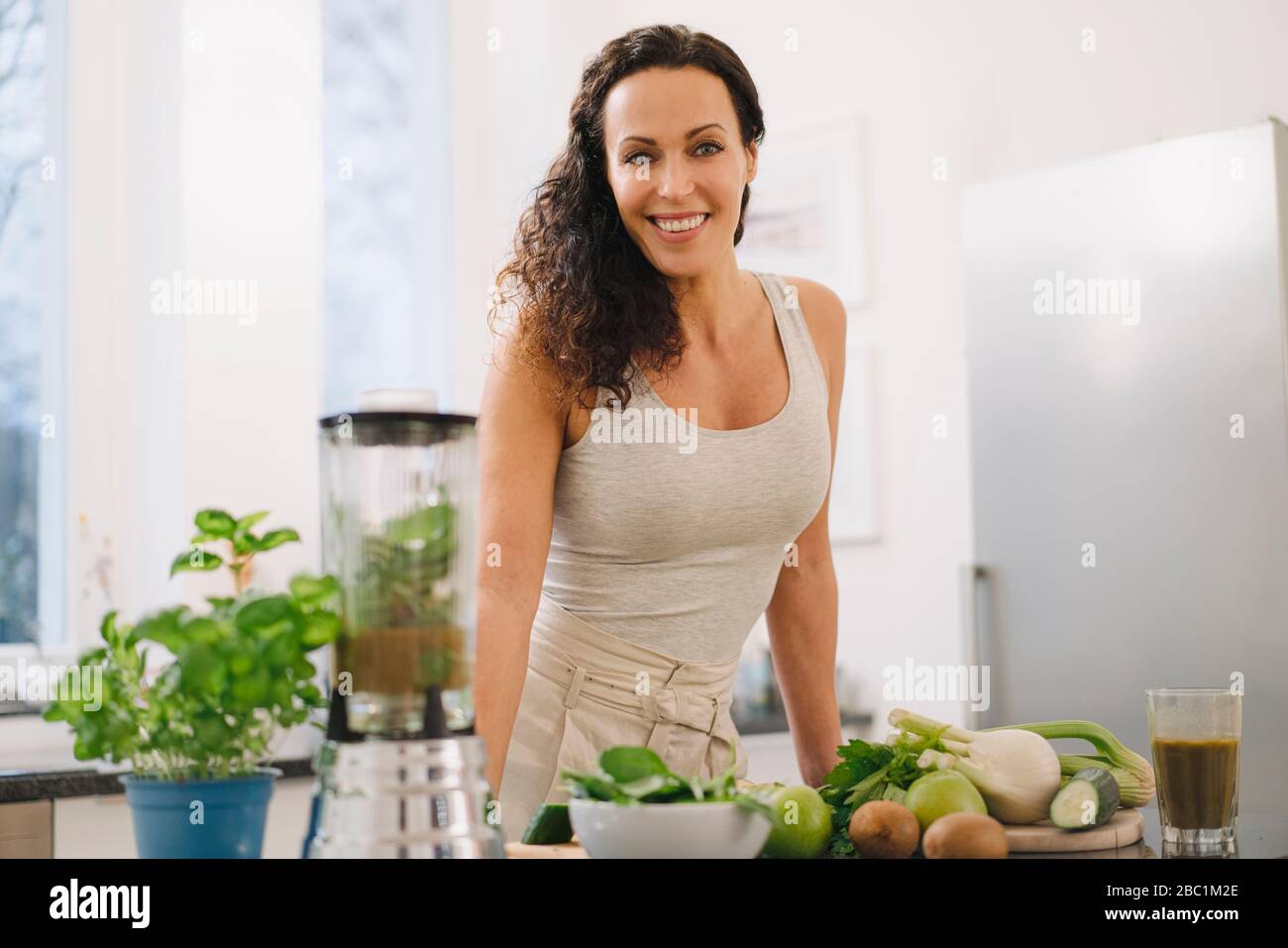 Mujer de pie en la cocina, preparar batidos saludables Foto de stock