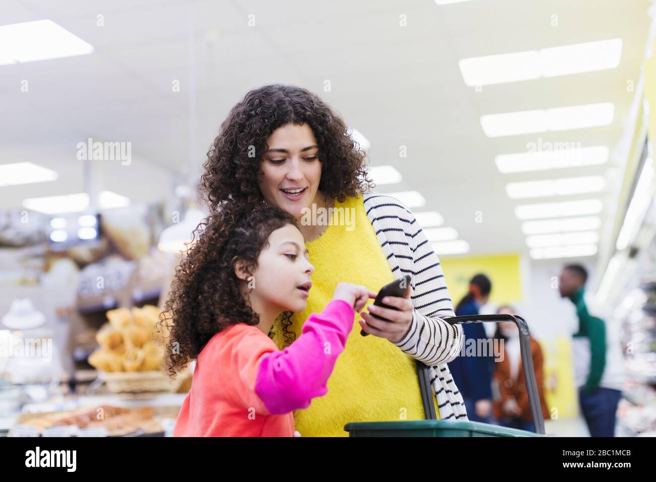 Madre e hija con teléfono inteligente de compras en el supermercado Foto de stock