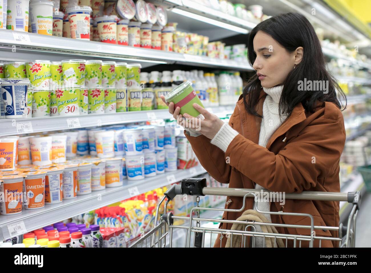 Mujer joven leyendo la etiqueta en el contenedor en el supermercado Foto de stock