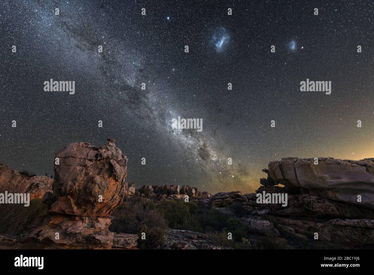 Una hermosa fotografía del cielo nocturno que muestra la vía Láctea y el centro galáctico, las Nubes Magallanes, con rocas dramáticas en primer plano, tomadas en el Foto de stock