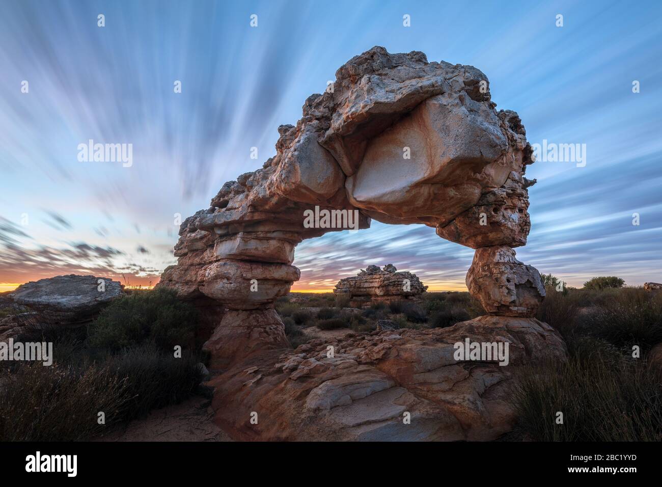 Una fotografía espectacular del paisaje de un increíble arco de roca antes del amanecer, con nubes en movimiento rápido contra un cielo azul, tomada en la montaña Cederberg Foto de stock