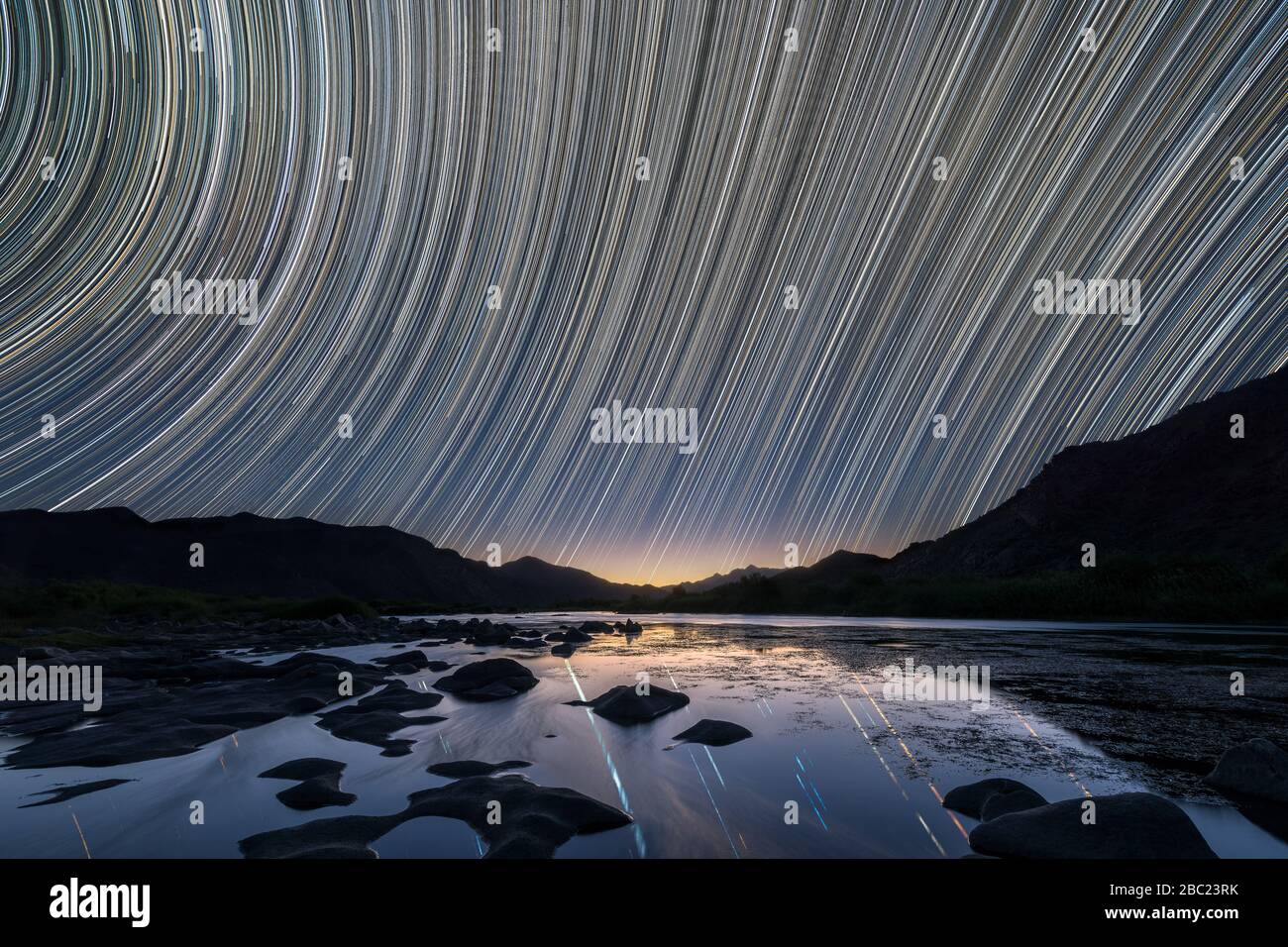 Un hermoso paisaje nocturno con senderos estelares que se reflejan en el río Orange y las montañas que se perfilan en el horizonte, tomado en el Richtersveld Na Foto de stock