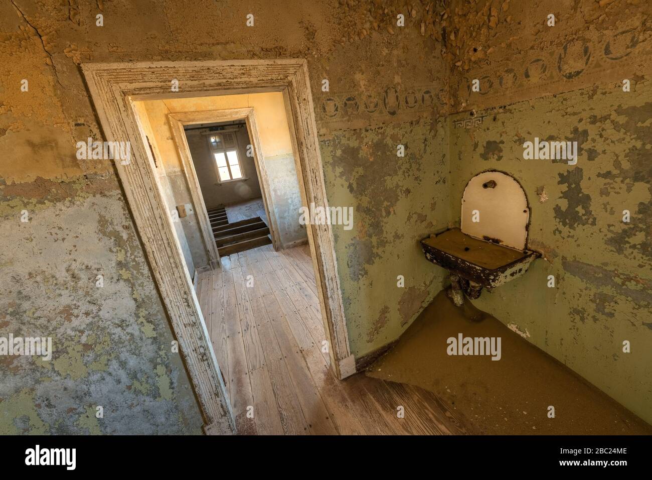 Una fotografía de un antiguo lavabo y una puerta que conduce a una habitación abandonada, tomada en la ciudad fantasma de Kolmanskop, Namibia. Foto de stock