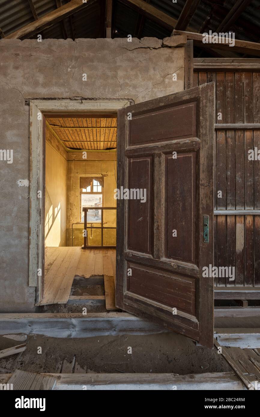 Una fotografía vertical dentro de una casa abandonada, con una puerta abierta enmarcando otra habitación, tomada en la ciudad fantasma de Kolmanskop, Namibia. Foto de stock