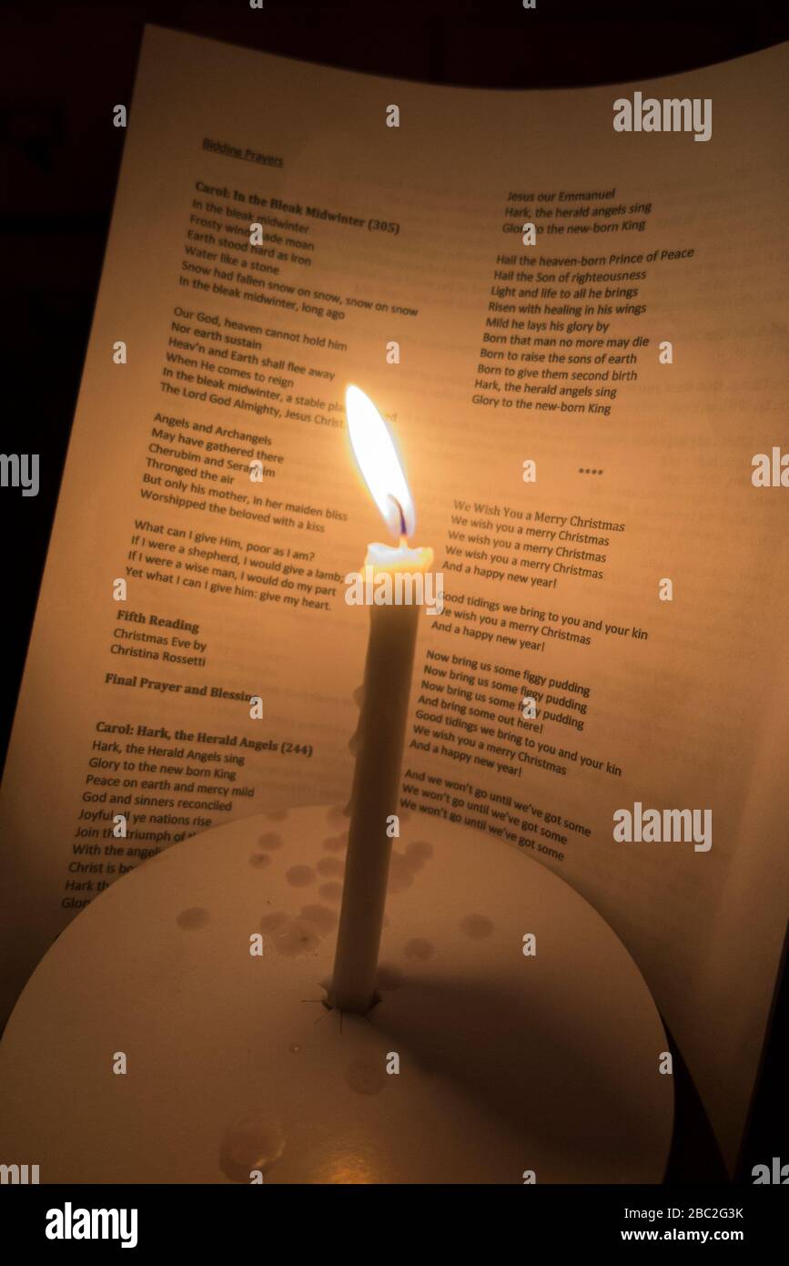 Vela de la iglesia con una llama ardiente fotografiada durante un concierto de Navidad del servicio de villancicos. Las palabras de los villancicos son visibles en la hoja de himnos detrás. Inglaterra Reino Unido (116) Foto de stock