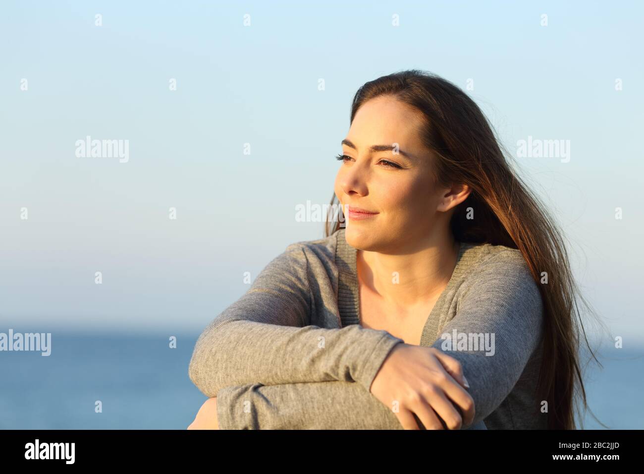 Mujer soltera segura viendo la puesta de sol sentada en la playa Foto de stock