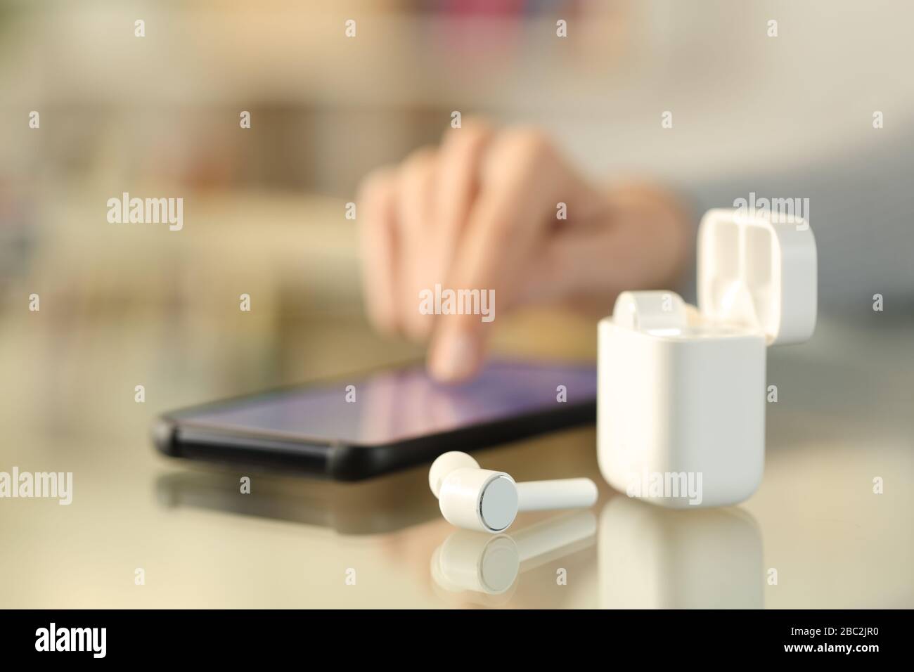 Primer plano de la mano de la chica con auriculares que se emparejan con el teléfono inteligente en un escritorio en casa Foto de stock