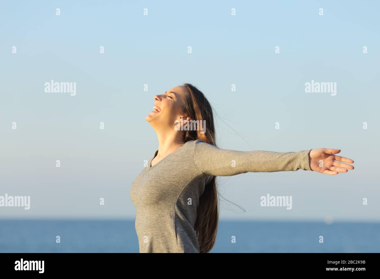 Vista lateral retrato de una mujer feliz estirando los brazos extendiendo la positividad en la playa Foto de stock