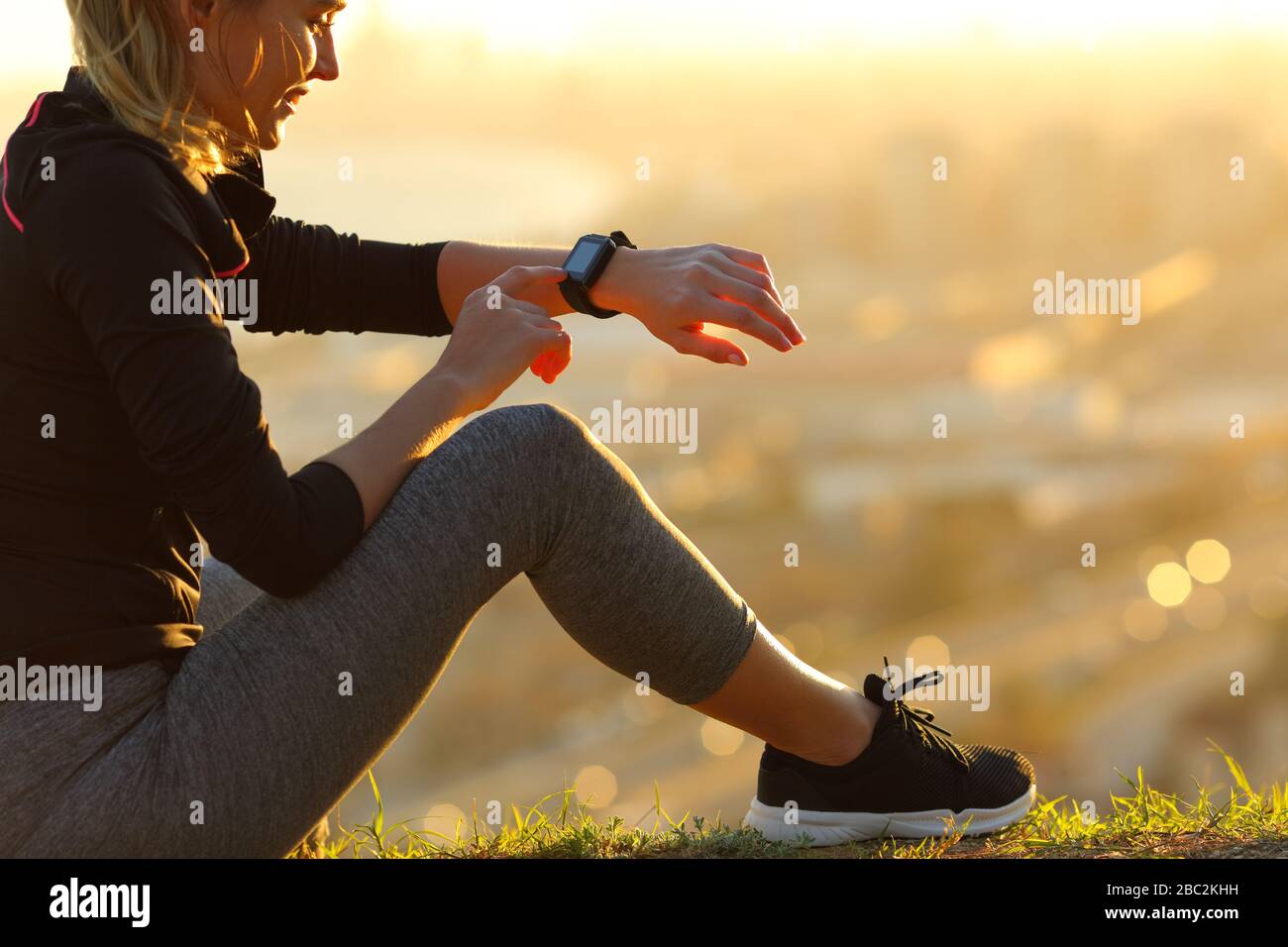Corredor sentado en el suelo comprobando smartwatch después de correr al atardecer Foto de stock