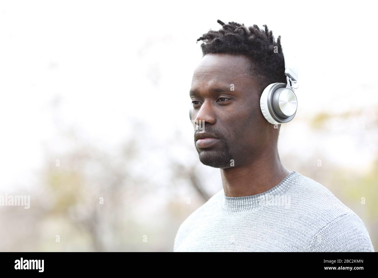 Hombre negro serio escuchando música con auriculares inalámbricos en  exteriores Fotografía de stock - Alamy