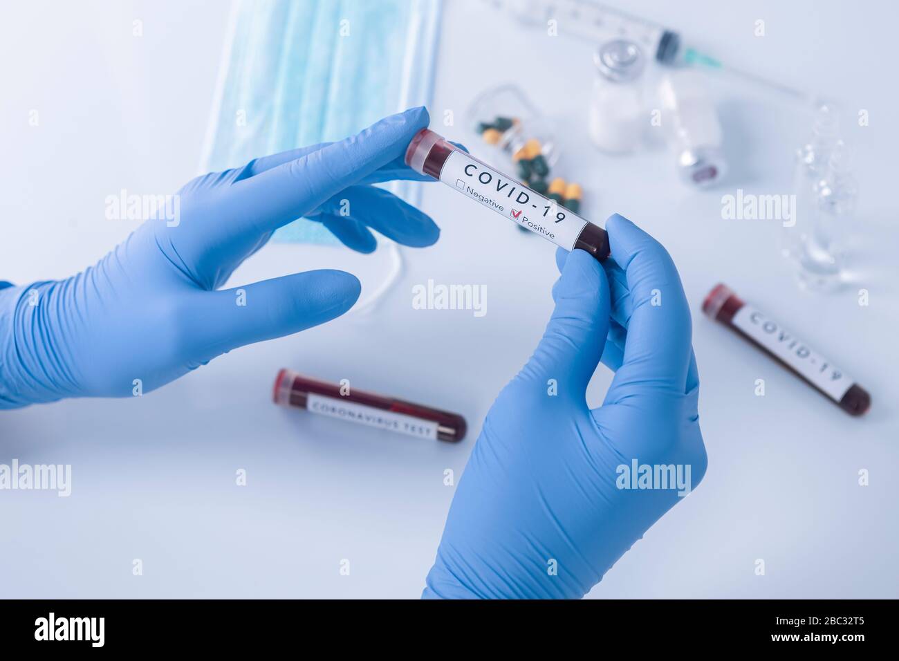 Manos de analistas con guantes protectores sosteniendo la sangre de la prueba del coronavirus COVID 19. Prueba de virus y concepto de investigación Foto de stock