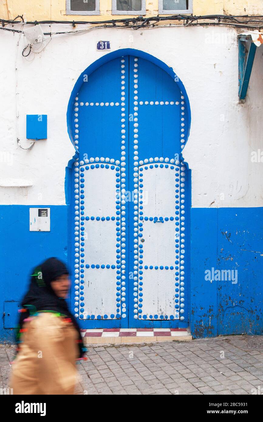 Una mujer pasa por una puerta azul y blanca en Tánger, Marruecos, África Foto de stock