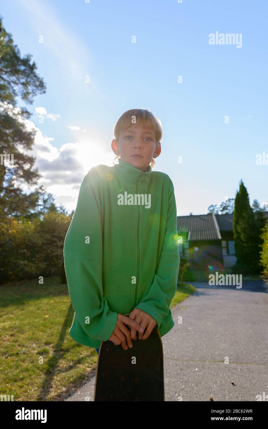 Joven niño guapo sosteniendo skateboard en el patio delantero Foto de stock