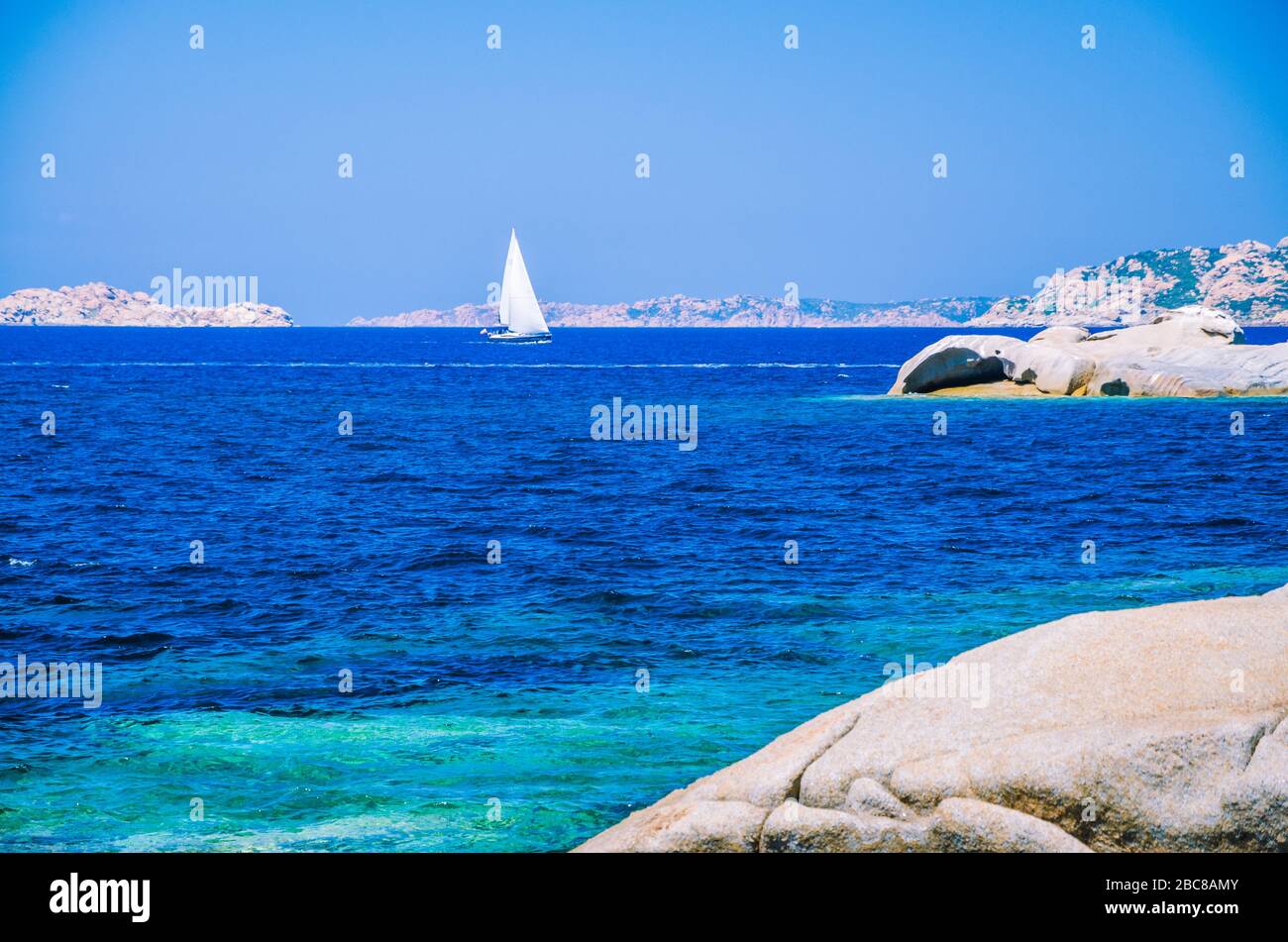 Blanco yate velero, entre rocas de granito en el mar, el agua azul impresionante, Cerdeña, Italia. Foto de stock