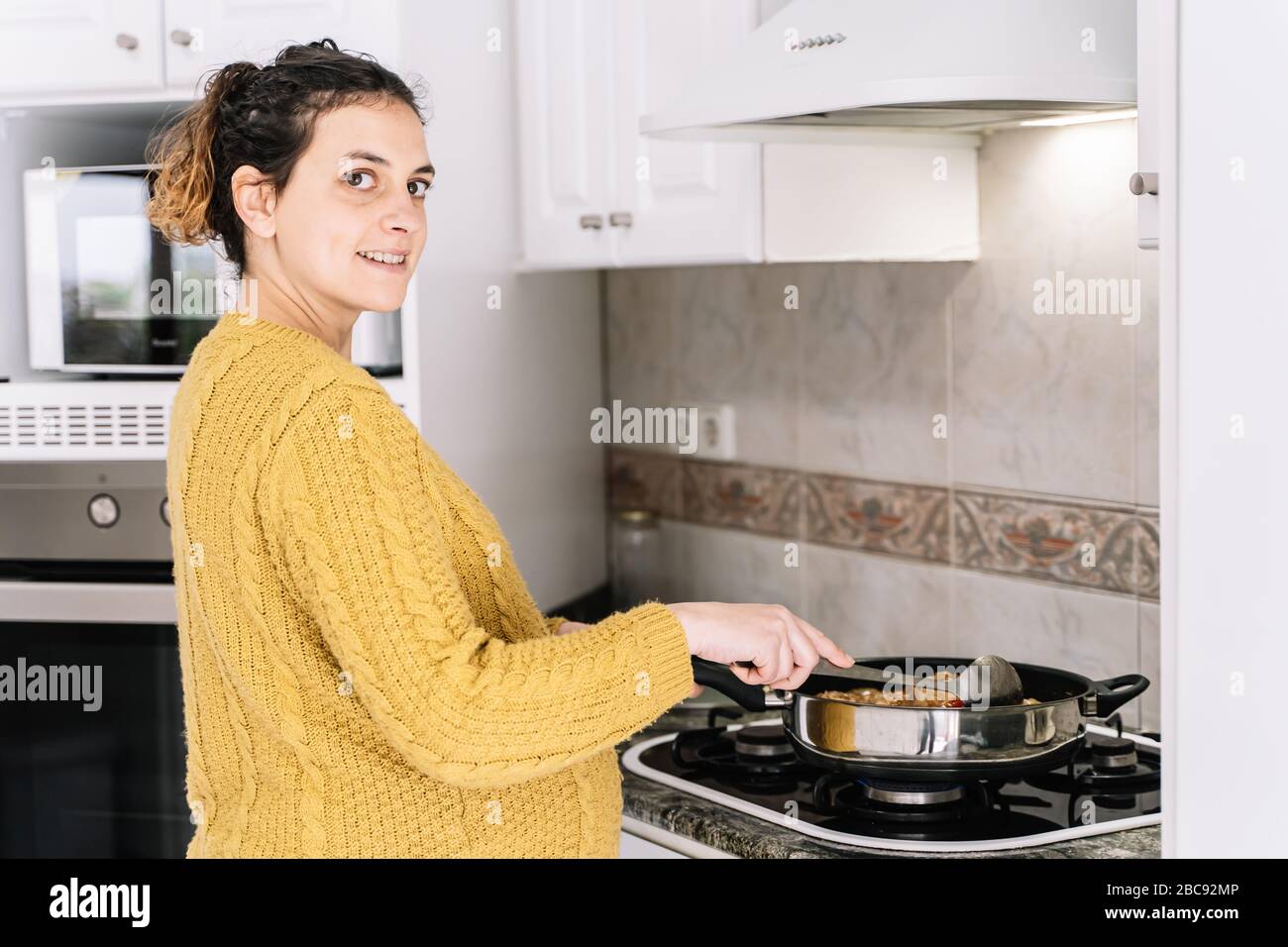 Mujer embarazada con un suéter amarillo cocinando de pie en una cocina  junto a un microondas sonriendo y girando la cara a la derecha Fotografía  de stock - Alamy