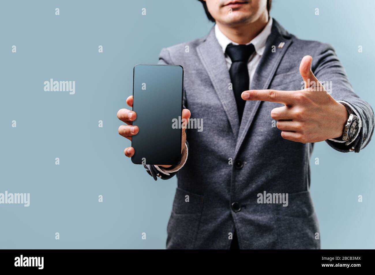 El joven sostiene el teléfono en la mano y señala con el dedo a la pantalla Foto de stock