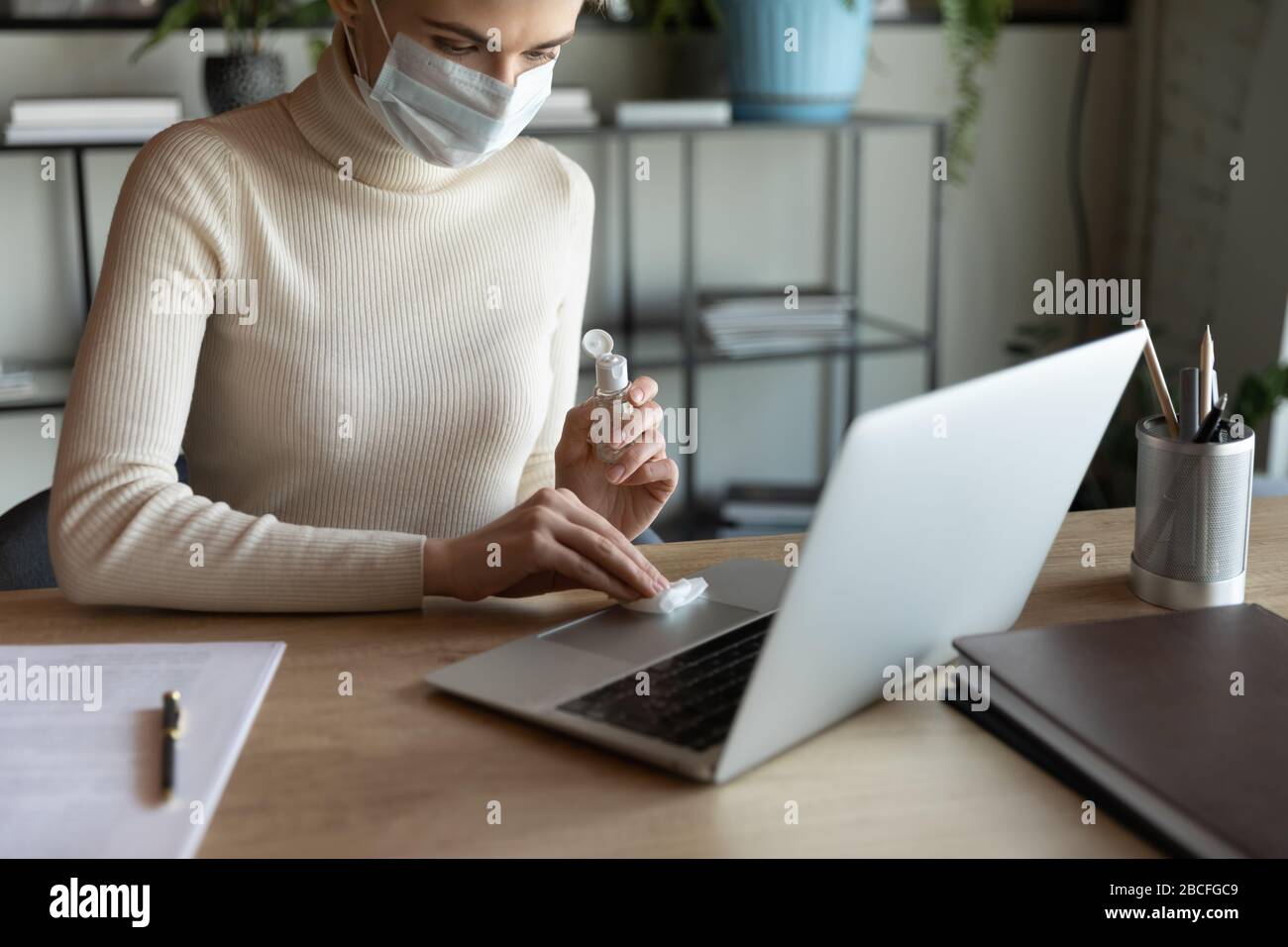 Mujer joven de 30 años con mascarilla facial y teclado esterilizante. Foto de stock