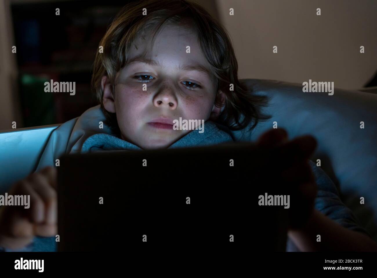Un niño juega juegos de ordenador en un tablet PC, en la habitación de sus hijos, en la cama, Foto de stock