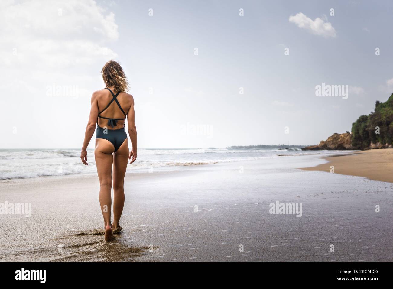 Rubia surfista chica con un traje de baño azul caminando en la playa en una poderosa pose mirando romper las olas, sur de Sri lanka Foto de stock