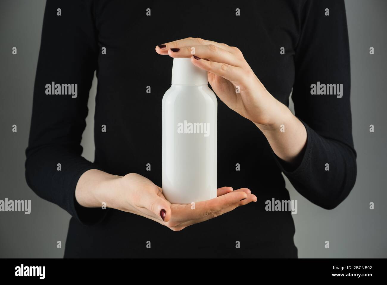 Botella blanca genérica en manos femeninas contra fondo con poca luz. Fotografía de productos, botella de plástico en blanco con espacio para texto de Marca o logotipo Foto de stock