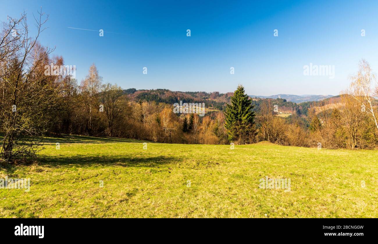 Paisaje montañoso sobre la ciudad de Turzovka en Eslovaquia con prados, colinas, bosque devastado por el escarabajo de la corteza y asentamiento disperso durante el día de primavera w Foto de stock