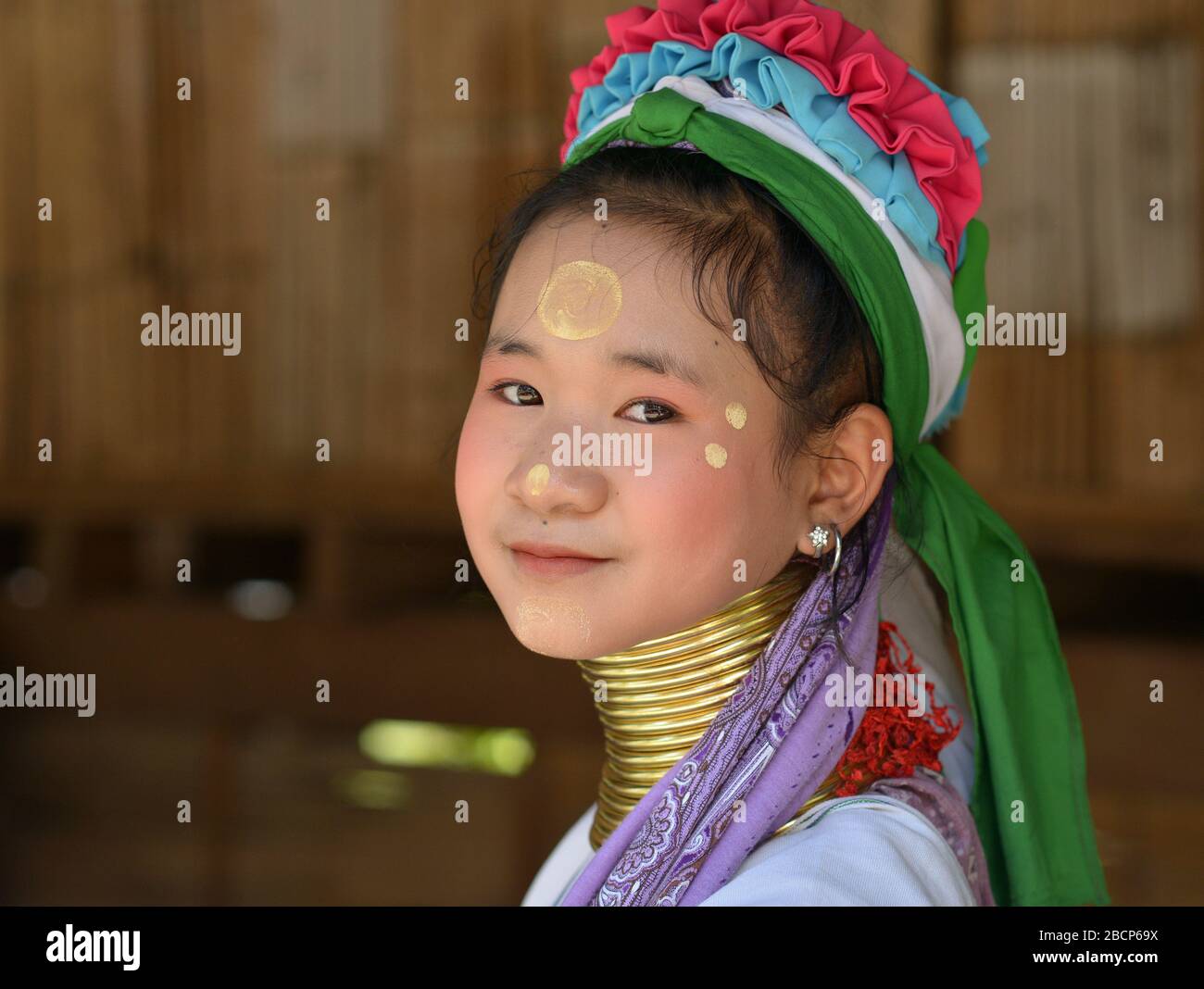 Bastante tailandés / birmano de cuello largo Kayan pre-adolescente (“mujer jirafa”) con anillos tribales de latón cuello / bobinas y thanaka en su cara sonríe para la cámara. Foto de stock