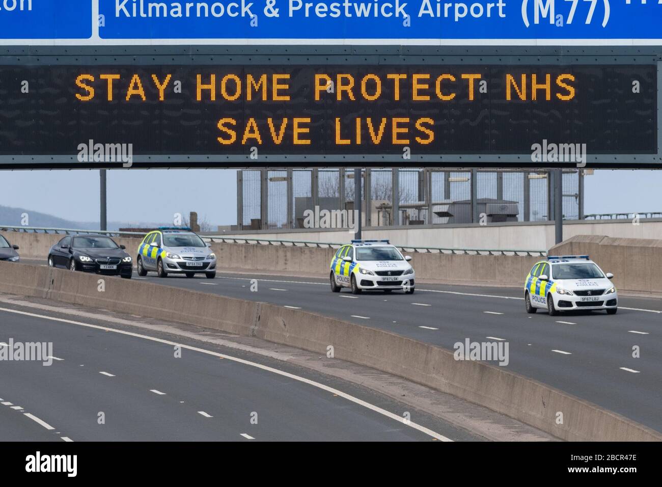 Coronavirus Reino Unido - medidas en Escocia - vehículos de policía que pasan bajo el signo "Stay Home Protect NHS Save Lives" en Glasgow Foto de stock