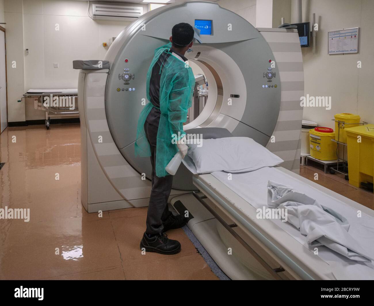 Máquina de tomografía computarizada (TC) en el Departamento de Radiología con un técnico de radiología que lleva equipo de protección personal (PPE) desinfectándolo Foto de stock