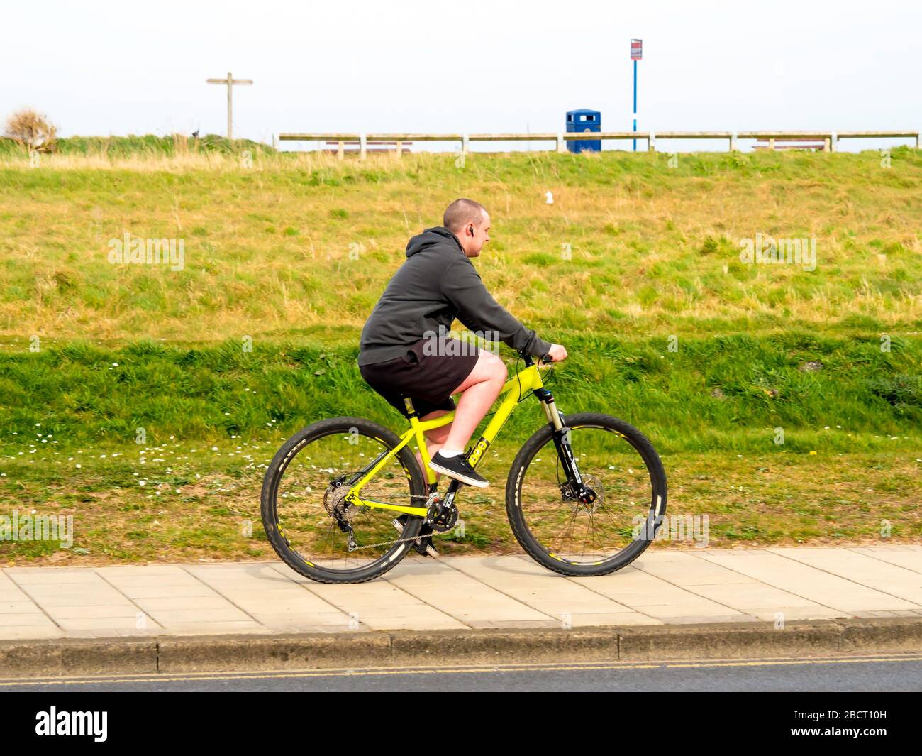 Un joven montando una bicicleta amarilla fuera de carretera en una pista de ciclismo con un banco de hierba detrás de él Foto de stock
